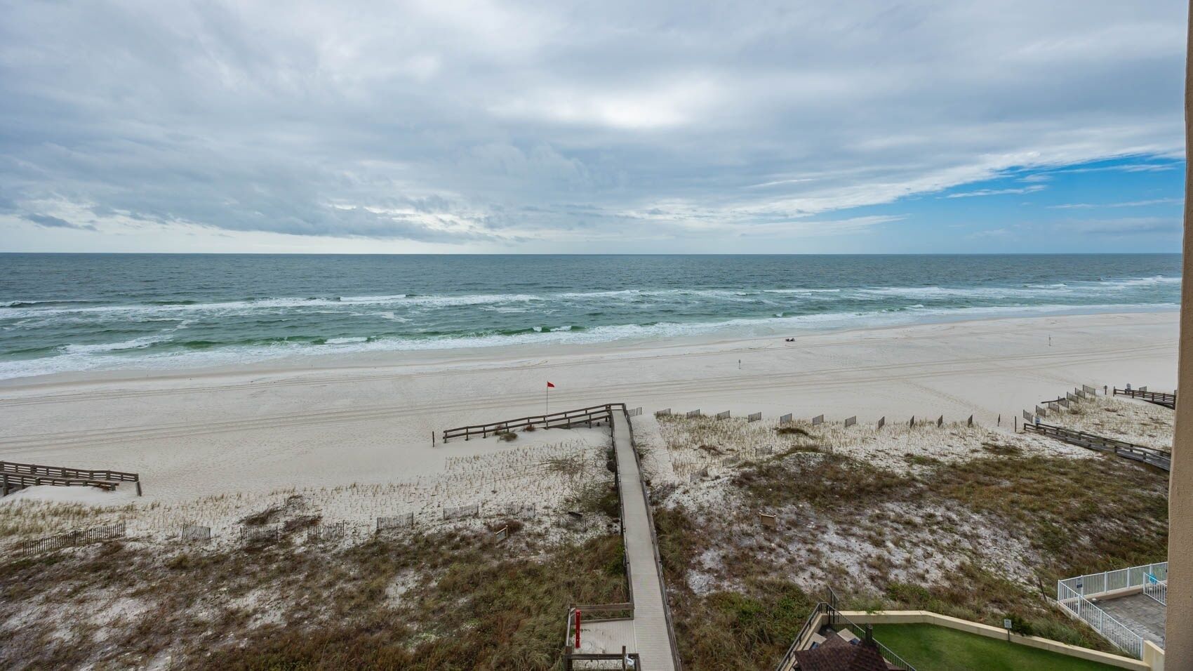 A beach with a wooden walkway leading to the water, a sandy beach, and a cloudy sky.