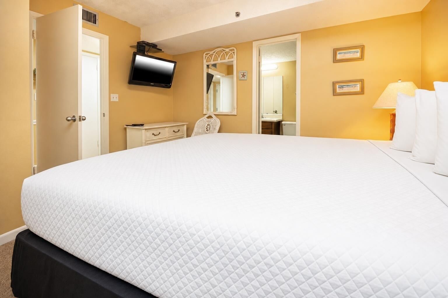 Una habitación de hotel con una cama grande, un televisor en la pared, un aparador y un espejo.