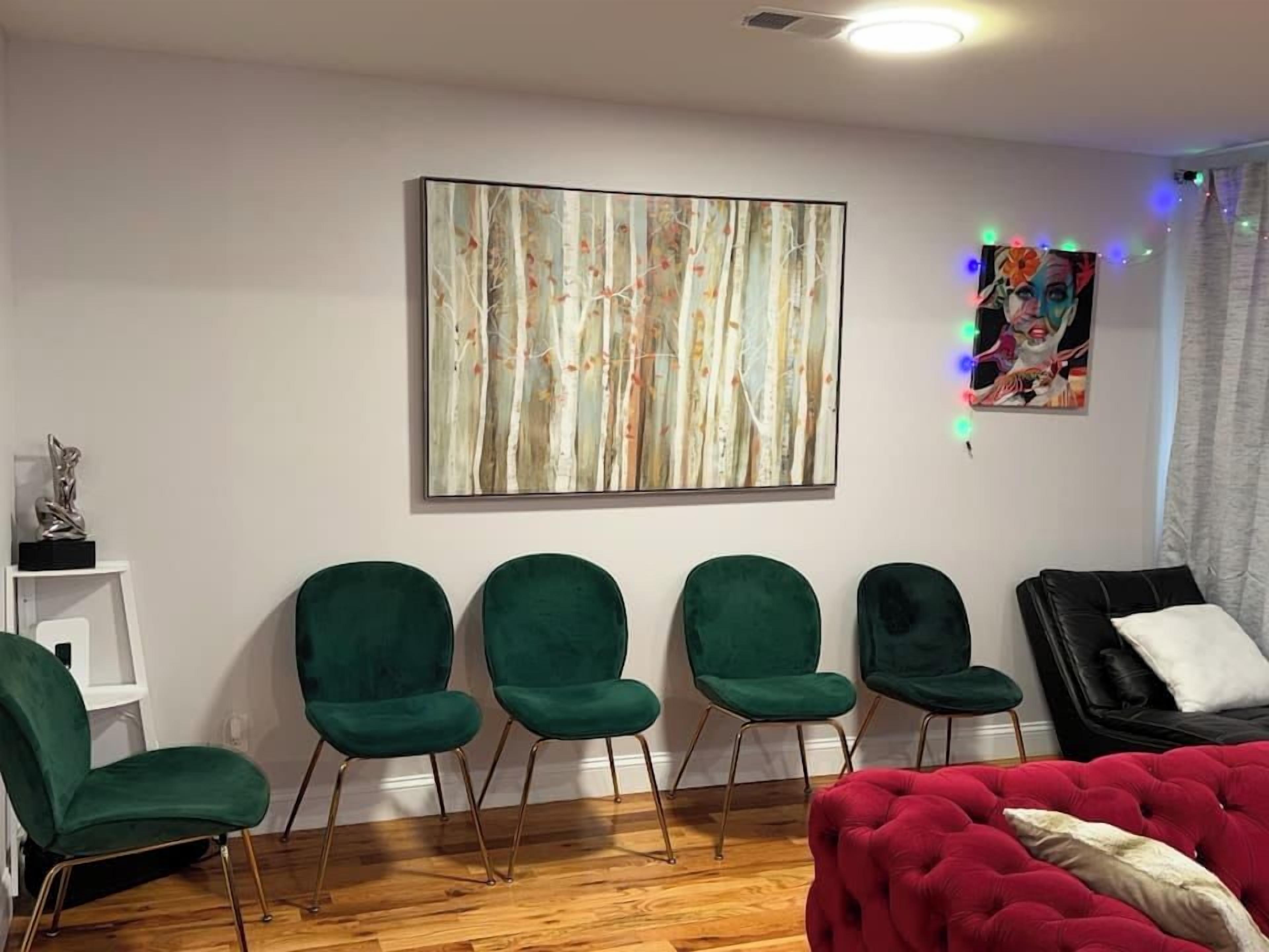 Una habitación con un cuadro abstracto grande, un sofá rojo y cuatro sillas verdes.