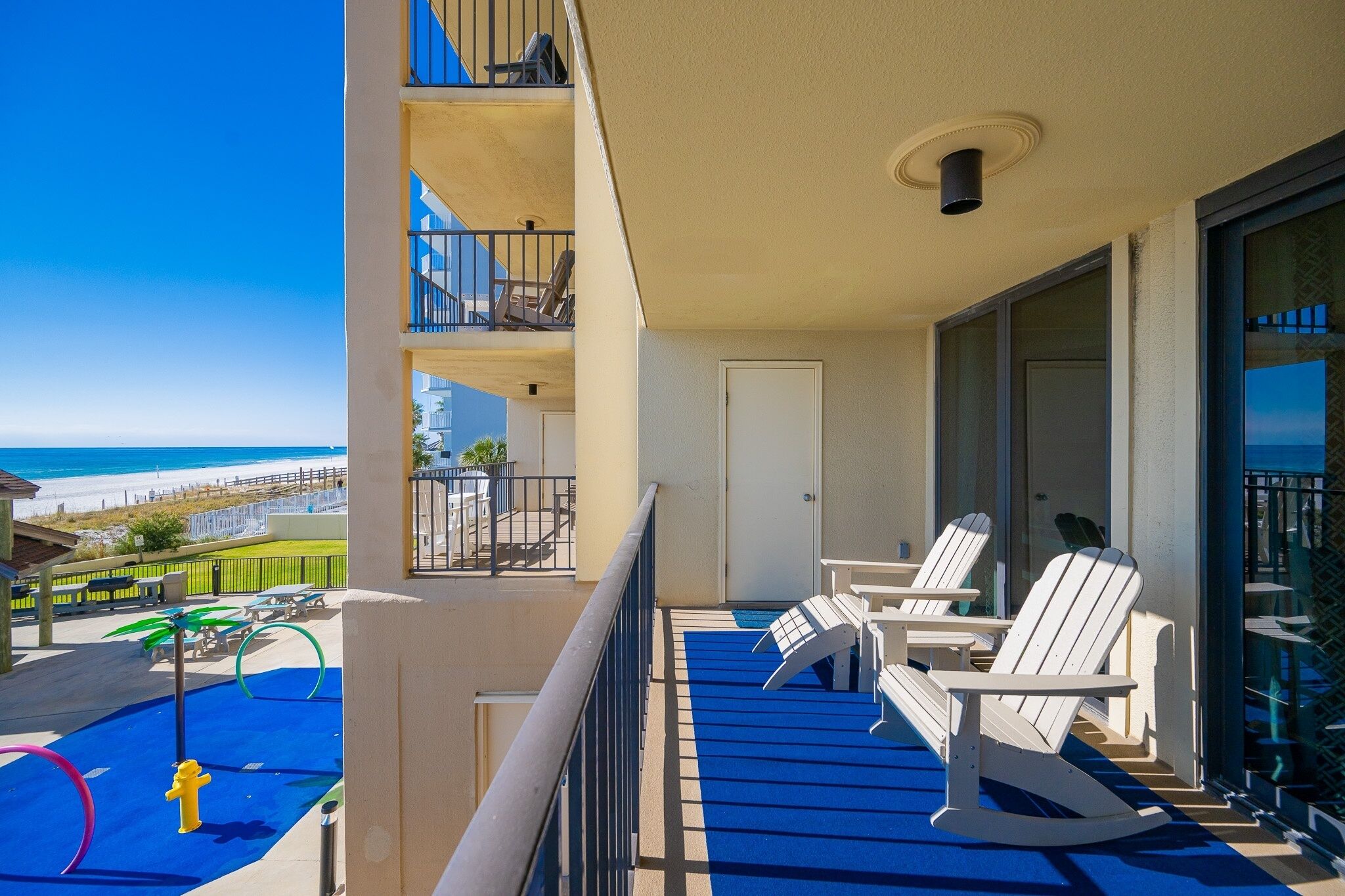 Un balcon avec des fauteuils Adirondack blancs, un espace de jeux bleu et une vue sur la plage.