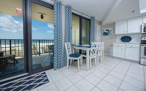 Un balcón con vista a la playa, un comedor con sillas y mesa blancas, y una cocina con armarios blancos y un microondas.