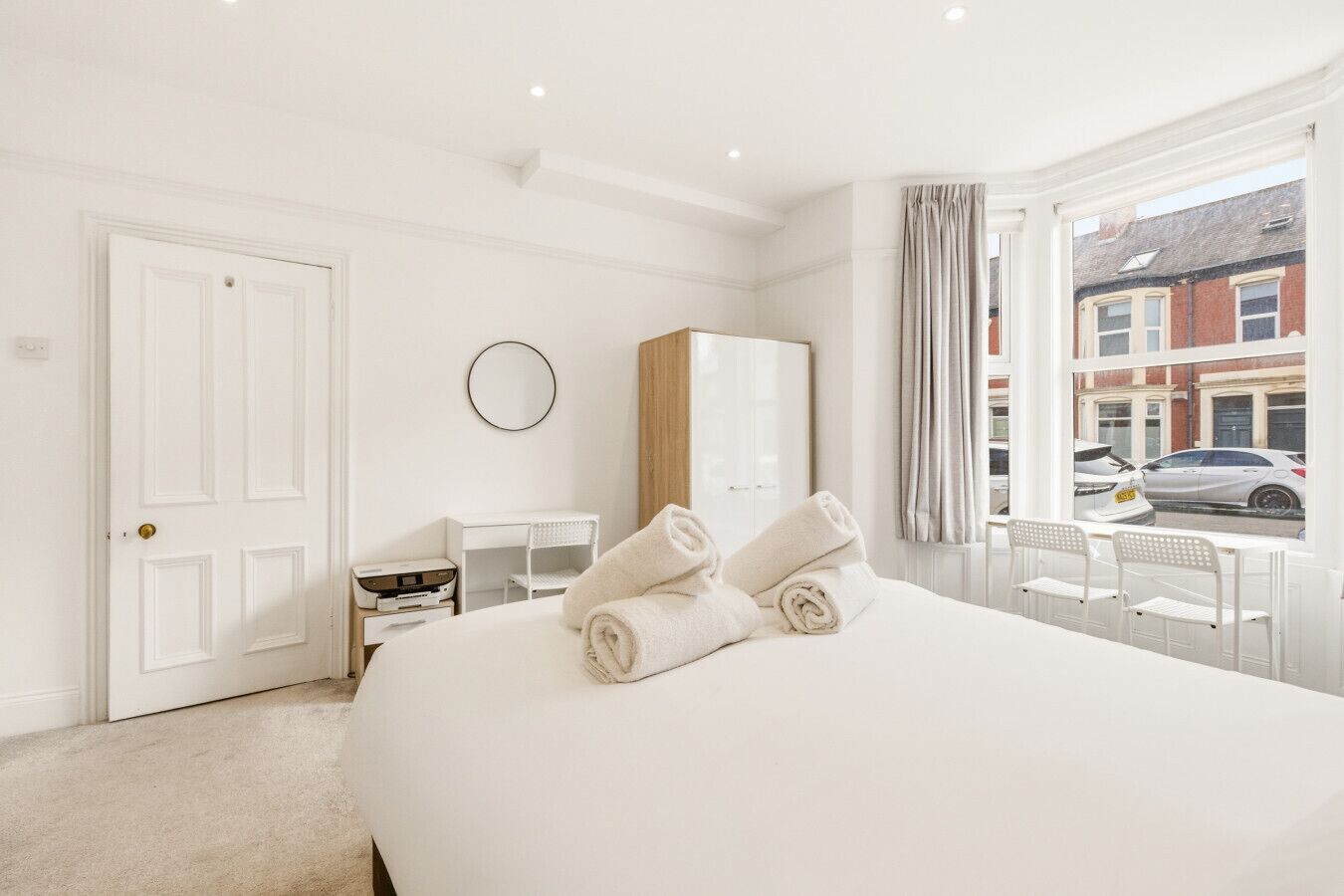 A hotel room with a large bed, a desk, a wardrobe, and a view of the street.