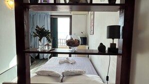 A hotel room with a bed, a table with fruit, a bottle, and a view of the outside. - Seafront Studio Apartment with Balcony (Podgora)