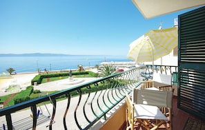 Ein Balkon mit Meerblick, ein gelb gestreifter Sonnenschirm und ein Stuhl.