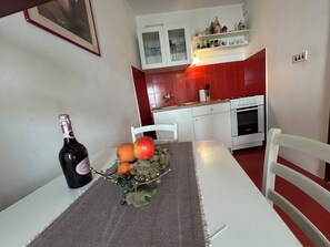 A kitchen with a dining table, a bottle of wine, and a fruit bowl. - Seafront Studio Apartment with Balcony (Podgora)