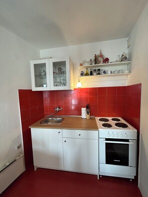 A compact kitchen with a sink, stove, and cabinets. - Seafront Studio Apartment with Balcony (Podgora)