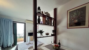 A bedroom with a bed, a desk with a bottle, a vase, and a shelf with decorative items. - Seafront Studio Apartment with Balcony (Podgora)