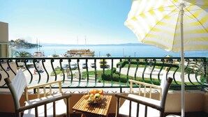 A balcony with a table holding fruit, a striped umbrella, and a view of the sea and vehicles. - Seafront Studio Apartment with Balcony (Podgora)