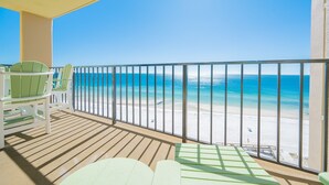 A balcony with a view of a beach, white chairs, and a wooden floor. - Phoenix I 1116 1 Bedroom Condo (Orange Beach)
