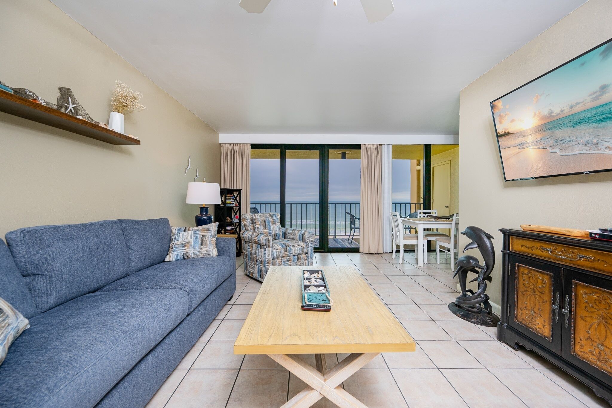 A living room with a sofa, a coffee table, a TV, and a view of the sea through large windows.