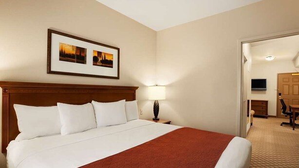 A hotel room with a large bed, a wooden headboard, a framed picture on the wall, a desk with a chair, and a television. - Country Inn & Suites by Radisson, Manchester Airport, NH (Bedford)