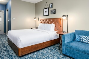 A hotel room with a large bed, a blue sofa, a wall-mounted lamp, and framed pictures. - Country Inn & Suites by Radisson, Manchester Airport, NH (Bedford)