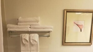 A bathroom with a toilet, a towel rack with folded towels, a framed picture on the wall, and a trash bin. - Country Inn & Suites by Radisson, Manchester Airport, NH (Bedford)