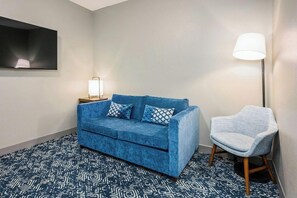 A room with a blue sofa, a patterned rug, a standing lamp, and a chair. - Country Inn & Suites by Radisson, Manchester Airport, NH (Bedford)