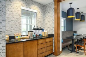 A modern kitchen with a stone backsplash, wooden cabinets, a built-in coffee station, and a seating area with a table and chairs. - Country Inn & Suites by Radisson, Manchester Airport, NH (Bedford)