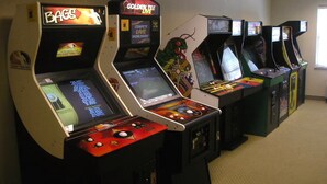 A row of arcade machines in a room with carpeted floors and plain walls. - Country Inn & Suites by Radisson, Manchester Airport, NH (Bedford)