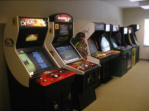 A row of arcade machines in a room with carpeted floors and plain walls. - Country Inn & Suites by Radisson, Manchester Airport, NH (Bedford)