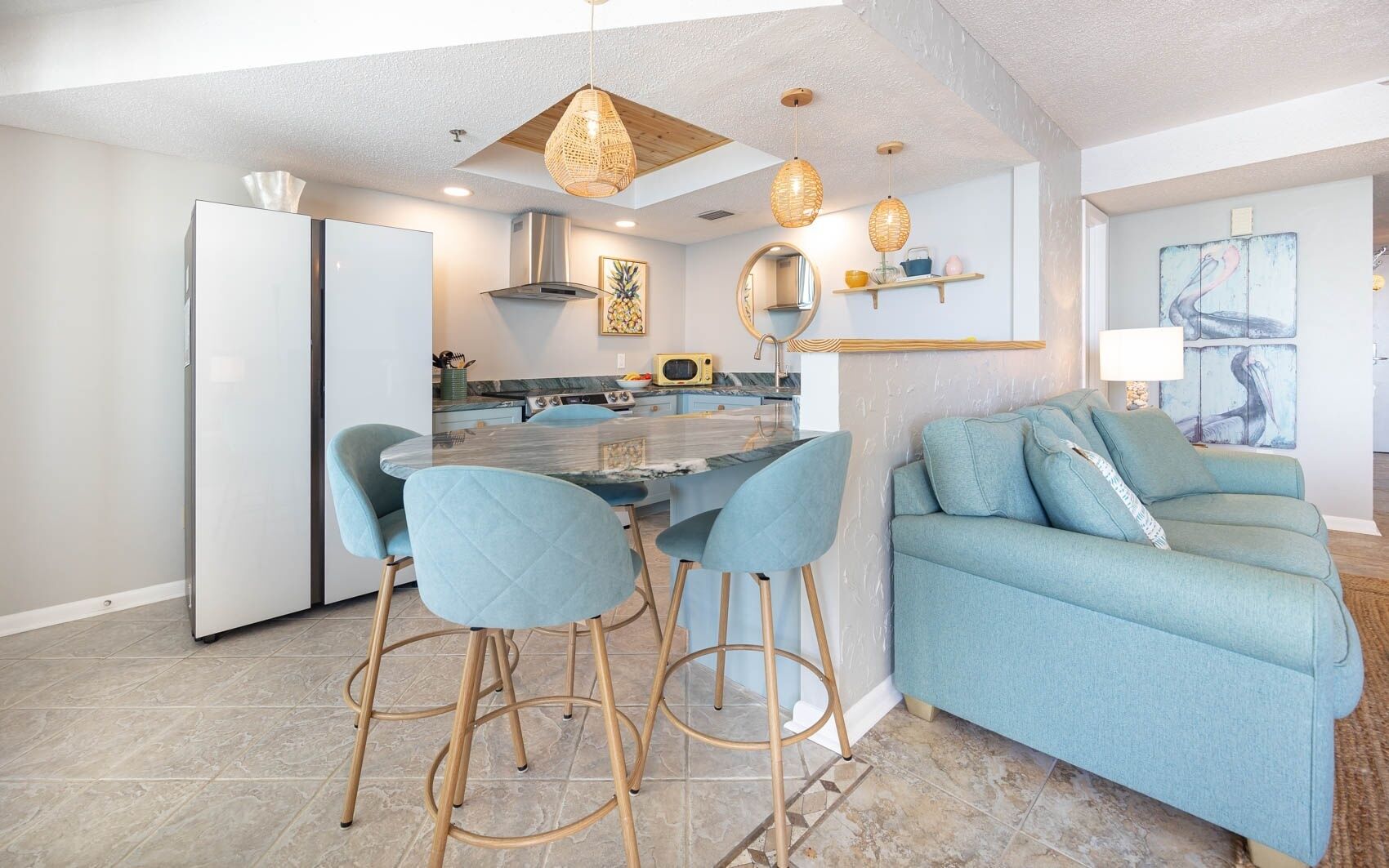 A modern kitchen with a central island, bar stools, and a light blue sofa.