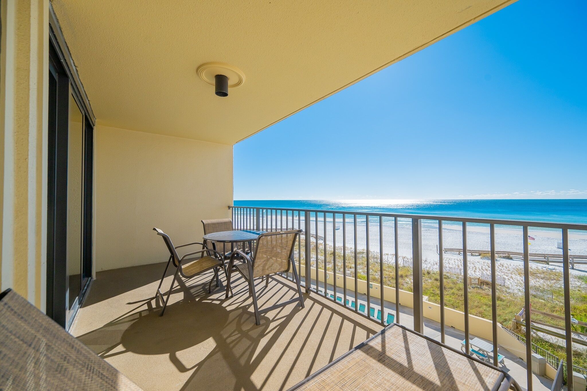A balcony with a table and chairs, a view of the beach, and a railing.