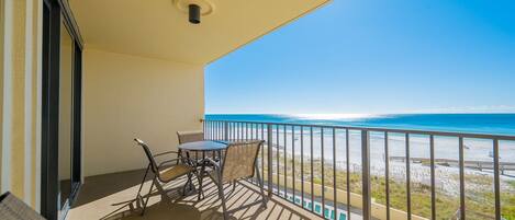 A balcony with a table and chairs, a view of the beach, and a railing.