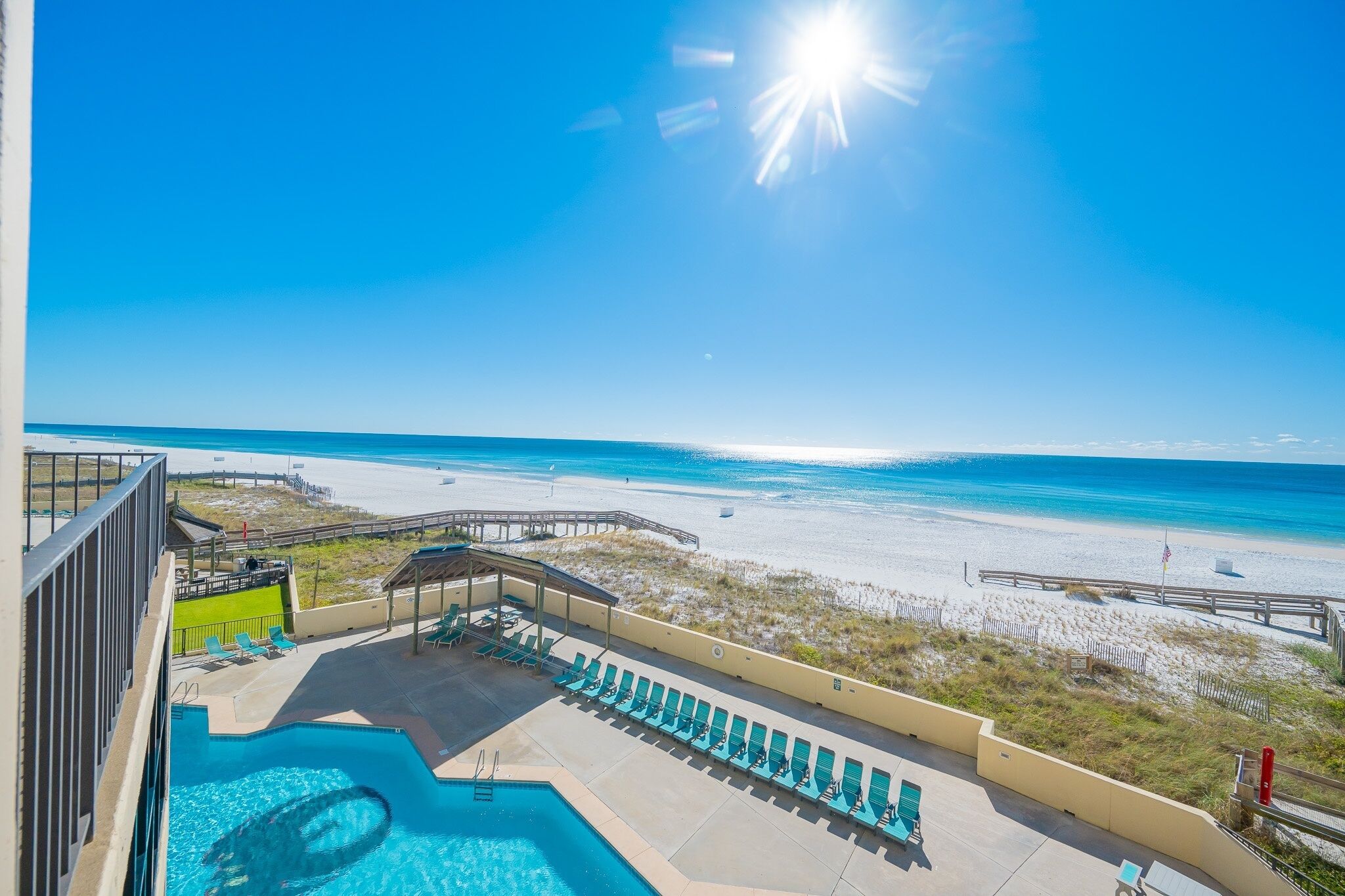 A pool area with lounge chairs, a wooden deck, and a view of the beach.