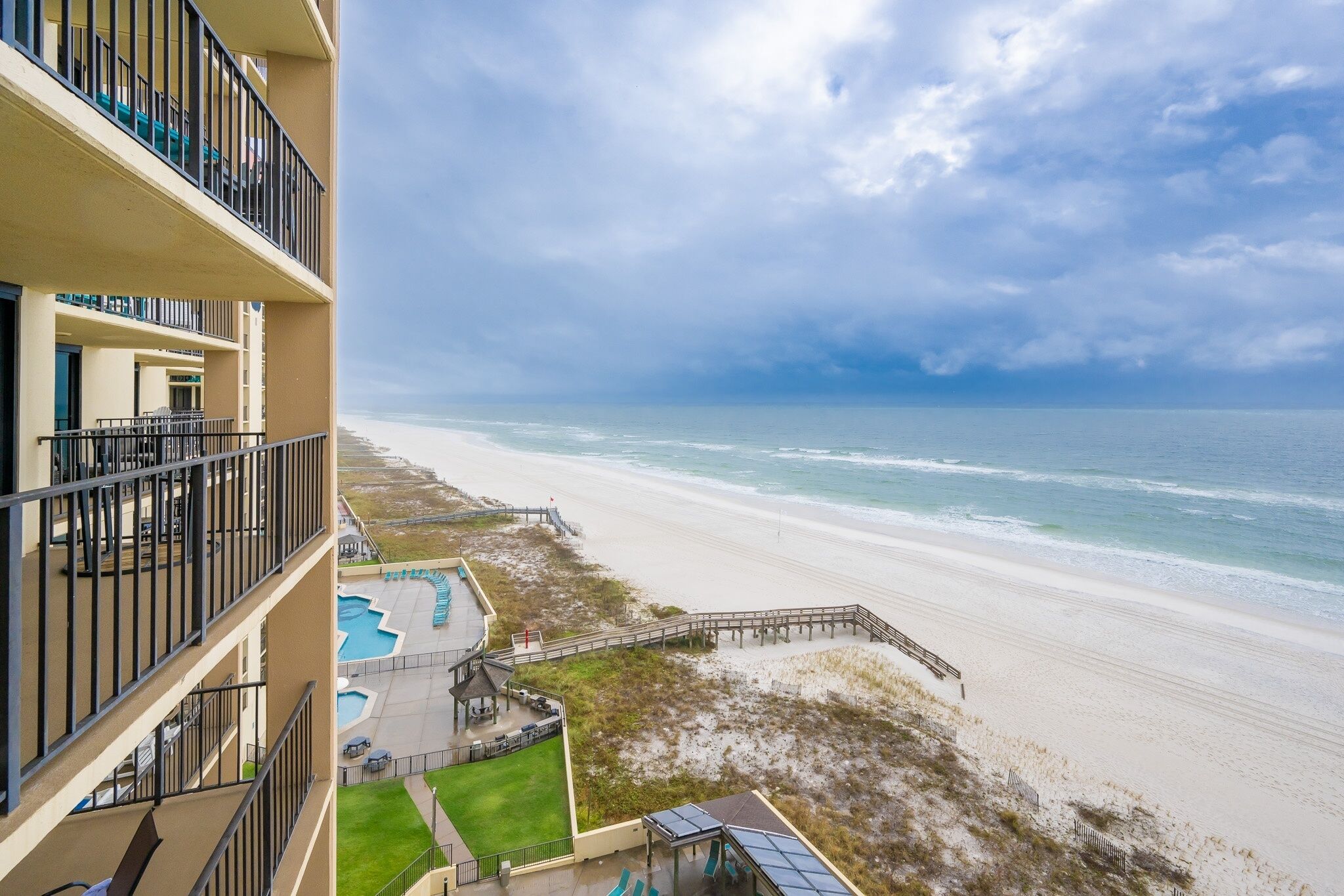 A beachfront hotel with balconies, a pool, and a boardwalk leading to the beach.