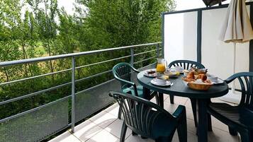 Un balcón con una mesa lista para el desayuno, rodeado de sillas, con vistas a un paisaje verde y exuberante.