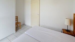 A hotel room with a bed, a chair, a door, and a nightstand with a lamp. - Residence Vacanceole Le Domaine du Green (Rivieres)
