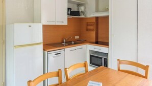 A compact kitchen with a refrigerator, microwave, and sink. There is a dining table with chairs. - Residence Vacanceole Le Domaine du Green (Rivieres)