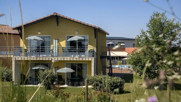 A yellow building with a balcony, outdoor seating, and a pool in the background. - Residence Vacanceole Le Domaine du Green (Rivieres)