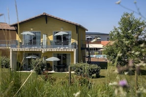 A yellow building with a balcony, outdoor seating, and a pool in the background. - Residence Vacanceole Le Domaine du Green (Rivieres)