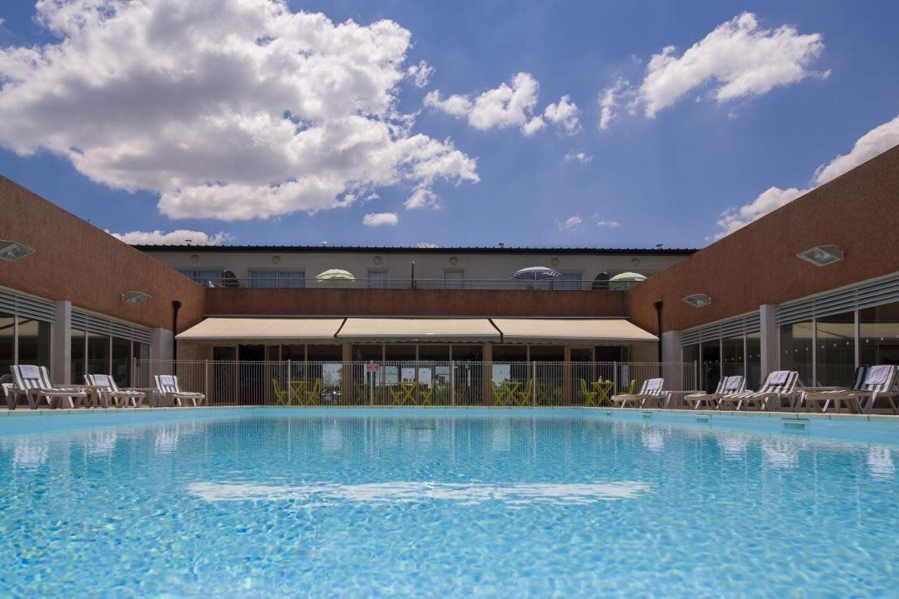Ein Pool mit Liegestühlen und einer überdachten Liegefläche, umgeben von einem Ziegelgebäude mit großen Fenstern.