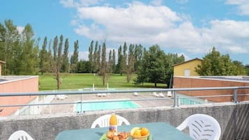 Un balcón con una mesa dispuesta para el desayuno, con vistas a una piscina y un área con césped.
