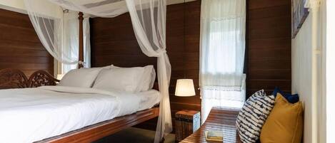 A bedroom with a wooden bed, a nightstand, a bedside table, a lamp, and a window with curtains.