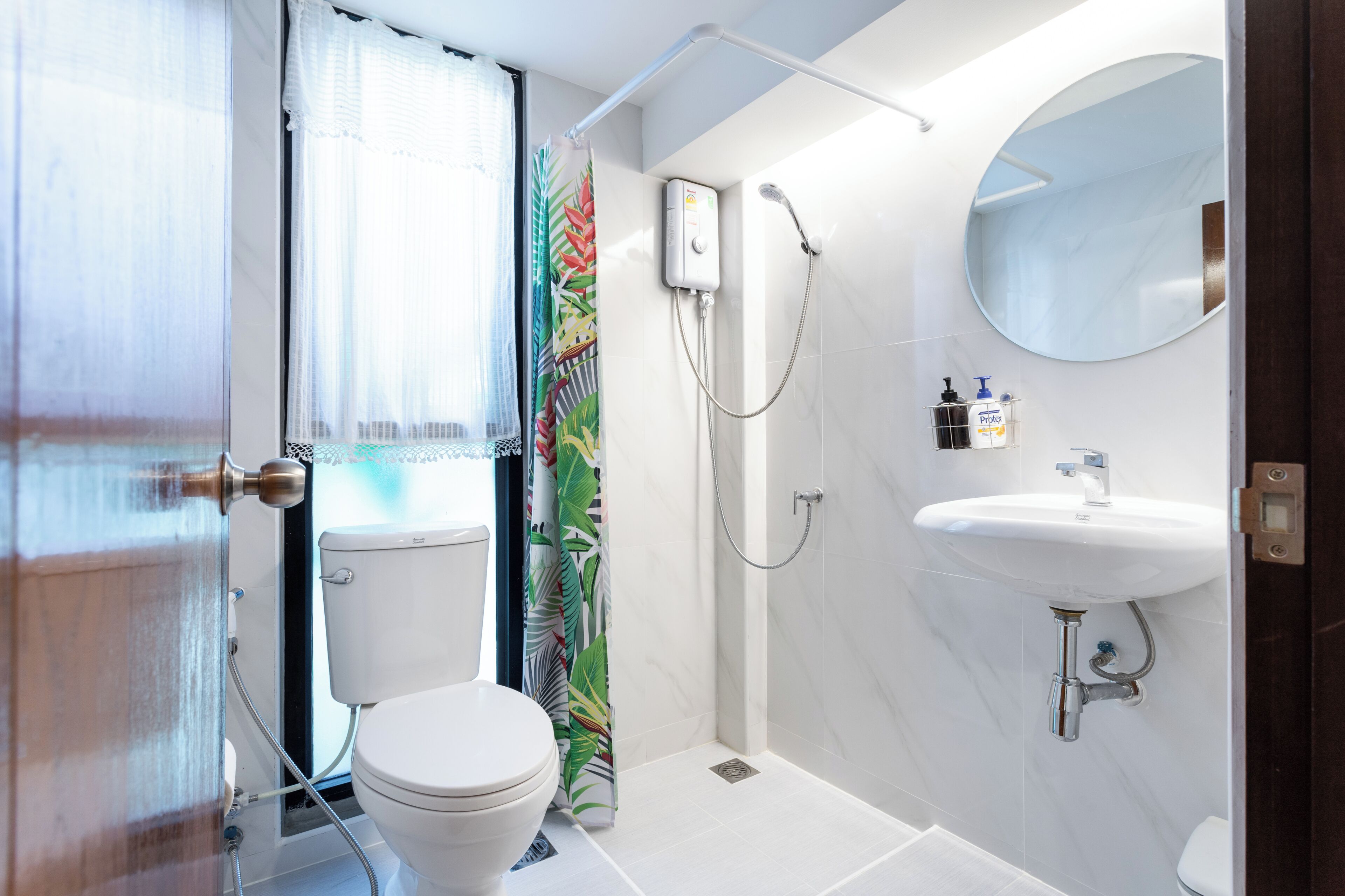 A bathroom with a toilet, shower, sink, and a mirror.