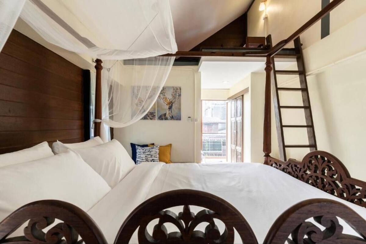 Un dormitorio con cama con dosel, cabecera de madera, escalera y vista al exterior.