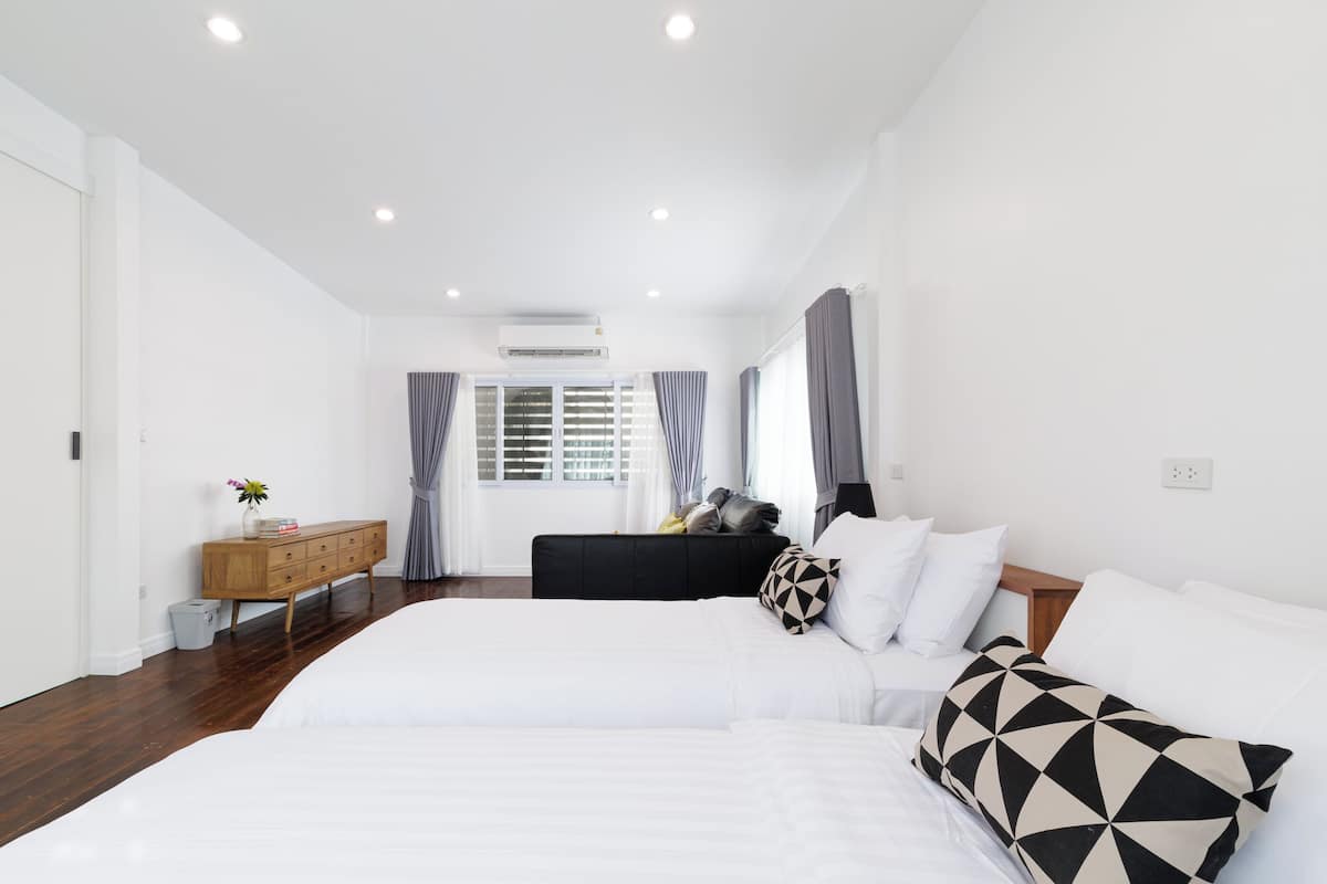 Una habitación de hotel con una cama grande, un aparador, una ventana con cortinas y un equipo de aire acondicionado.