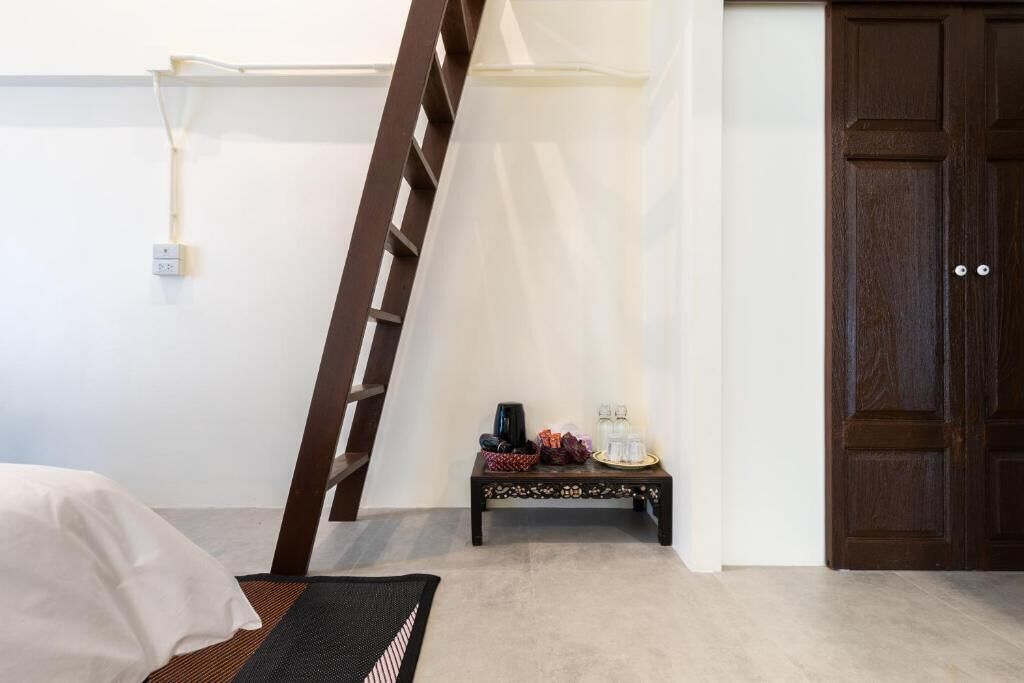 Una habitación con una cama, una escalera de madera, una mesita con objetos y una puerta de madera oscura.
