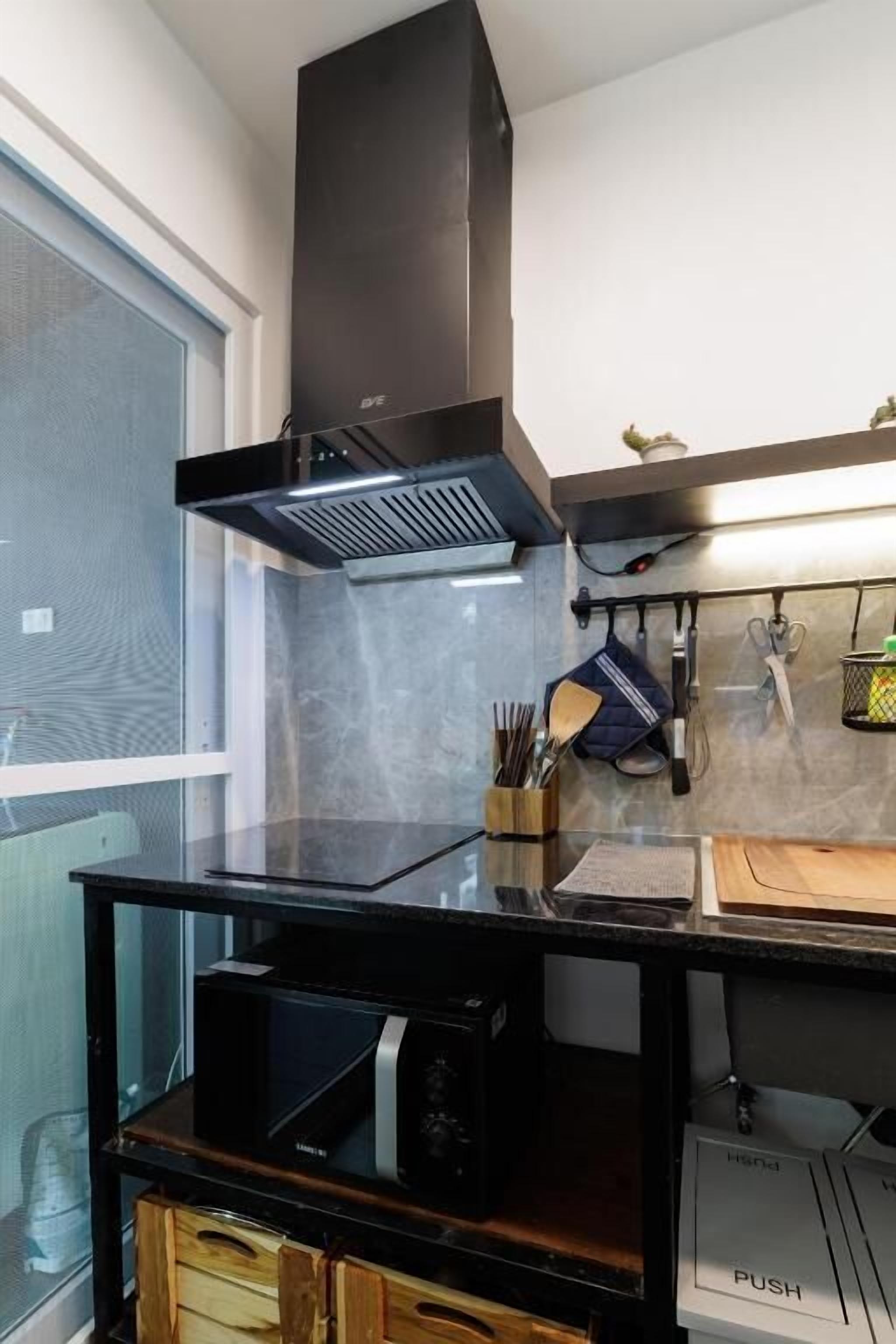 A modern kitchen with a black countertop, a built-in microwave, a black range hood, and a wooden cabinet below.