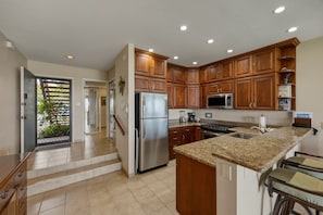 A kitchen with wooden cabinets, a stainless steel refrigerator, a microwave, and a granite countertop. - Napili Oceanfront 1br Condo Sleeps 4 - Unit B14 1 Bedroom Condo (Lahaina)