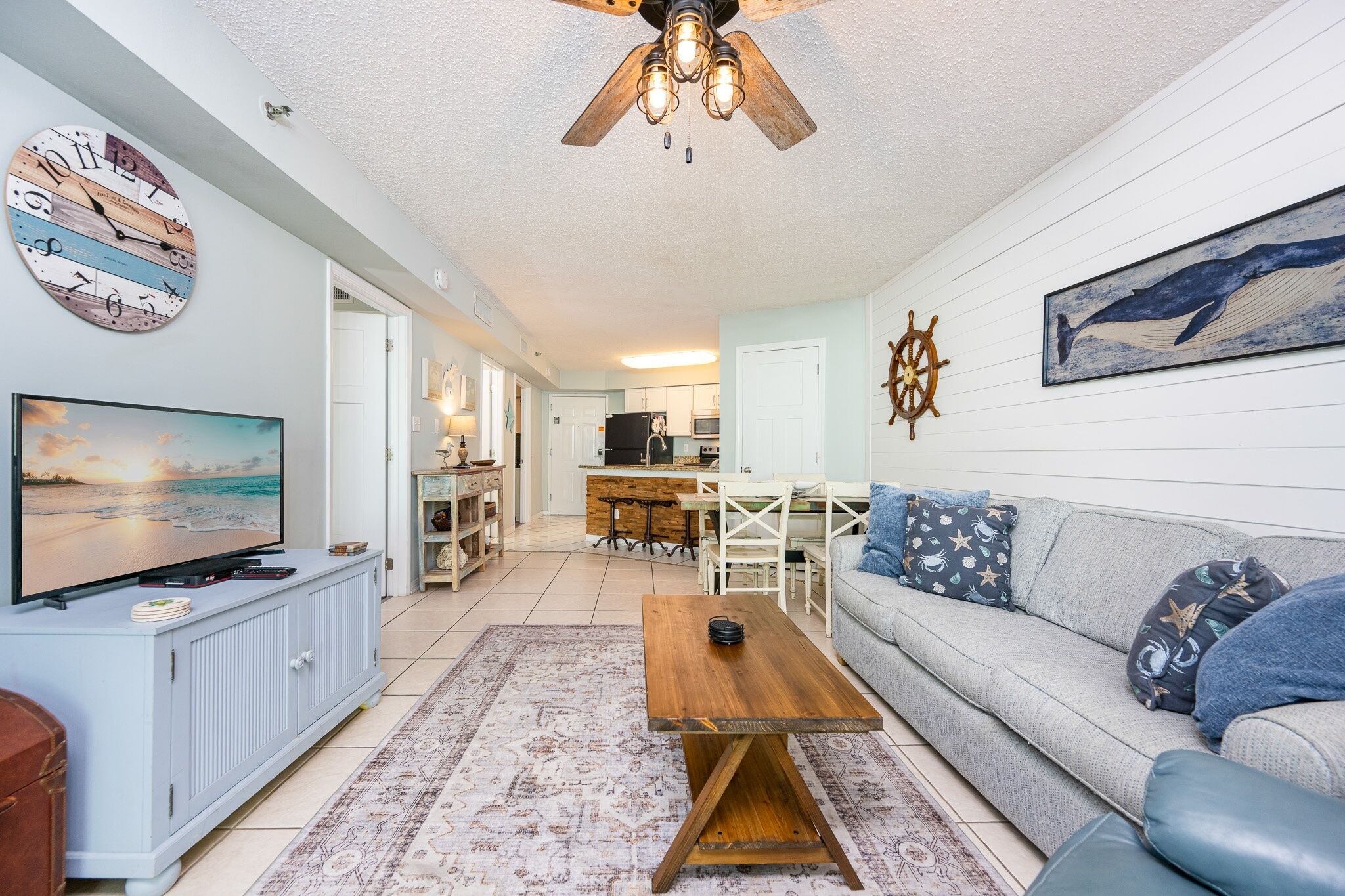 A living room with a television, a wooden coffee table, a sofa, and a ceiling fan.