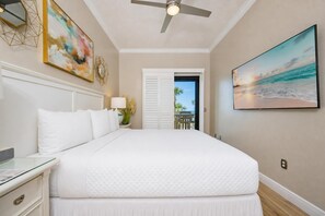A spacious bedroom with a large bed, a ceiling fan, a view of the ocean through a door, and artwork on the walls. - Phoenix Vi 6114 2 Bedroom Condo (Orange Beach)