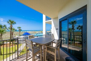Un balcón con mesa y sillas, con vista a una piscina y una playa.