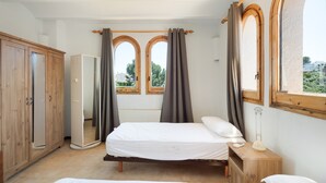 A bedroom with a bed, wooden wardrobe, mirror, and two windows with curtains. - House with Spacious Terrace and Private Barbecue (Begur)