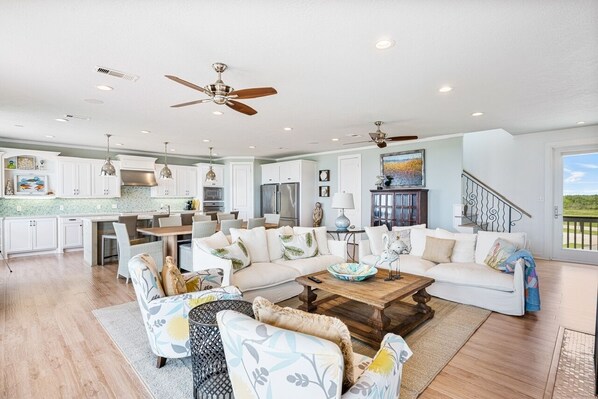 A spacious living area with a large sectional sofa, a coffee table, and a dining area with a kitchen in the background. - Dawn Treader 4 Bedroom Home (Port Bolivar)
