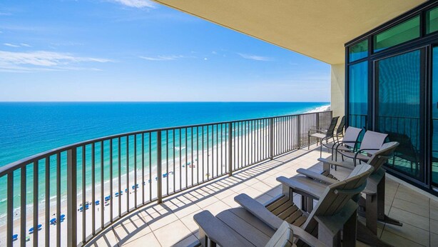 A balcony with a view of the ocean, outdoor seating, and a large window. - Phoenix West 1803 3 Bedroom Condo (Orange Beach)