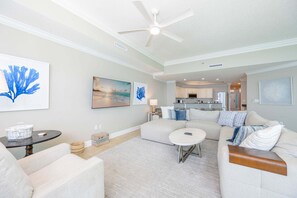 A living room with a ceiling fan, a sofa, a coffee table, and artwork on the walls. - Phoenix West 1803 3 Bedroom Condo (Orange Beach)