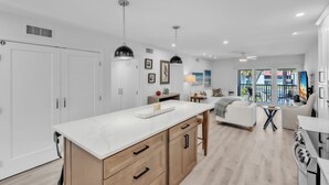Cocina moderna con encimera de mármol, armarios de madera, iluminación colgante y vistas al exterior.