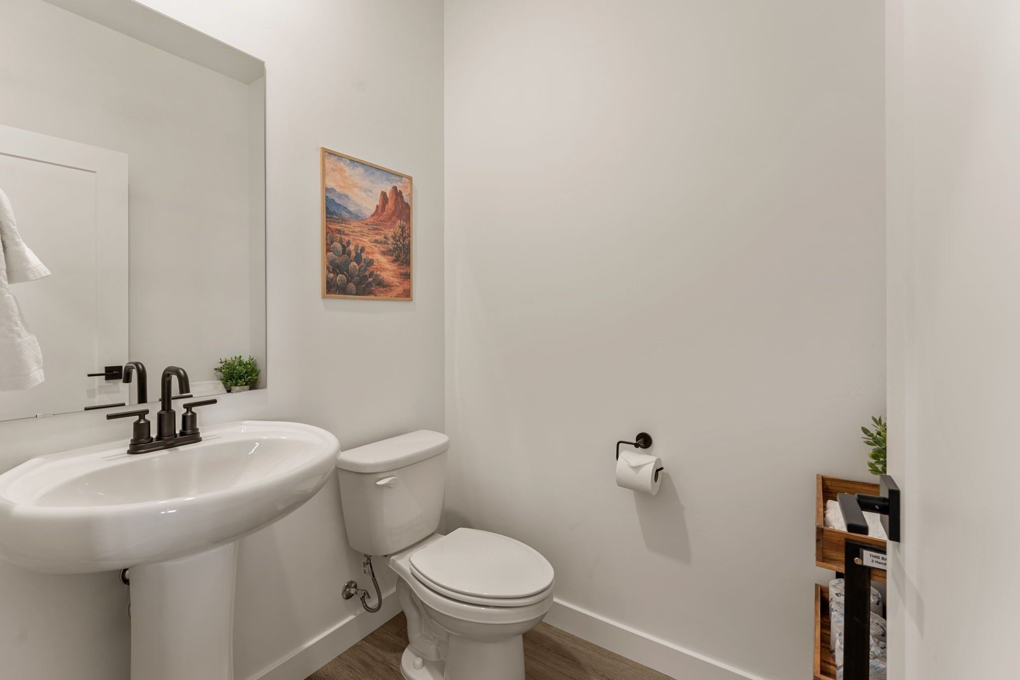 A bathroom with a white sink, toilet, and a painting of a desert landscape.