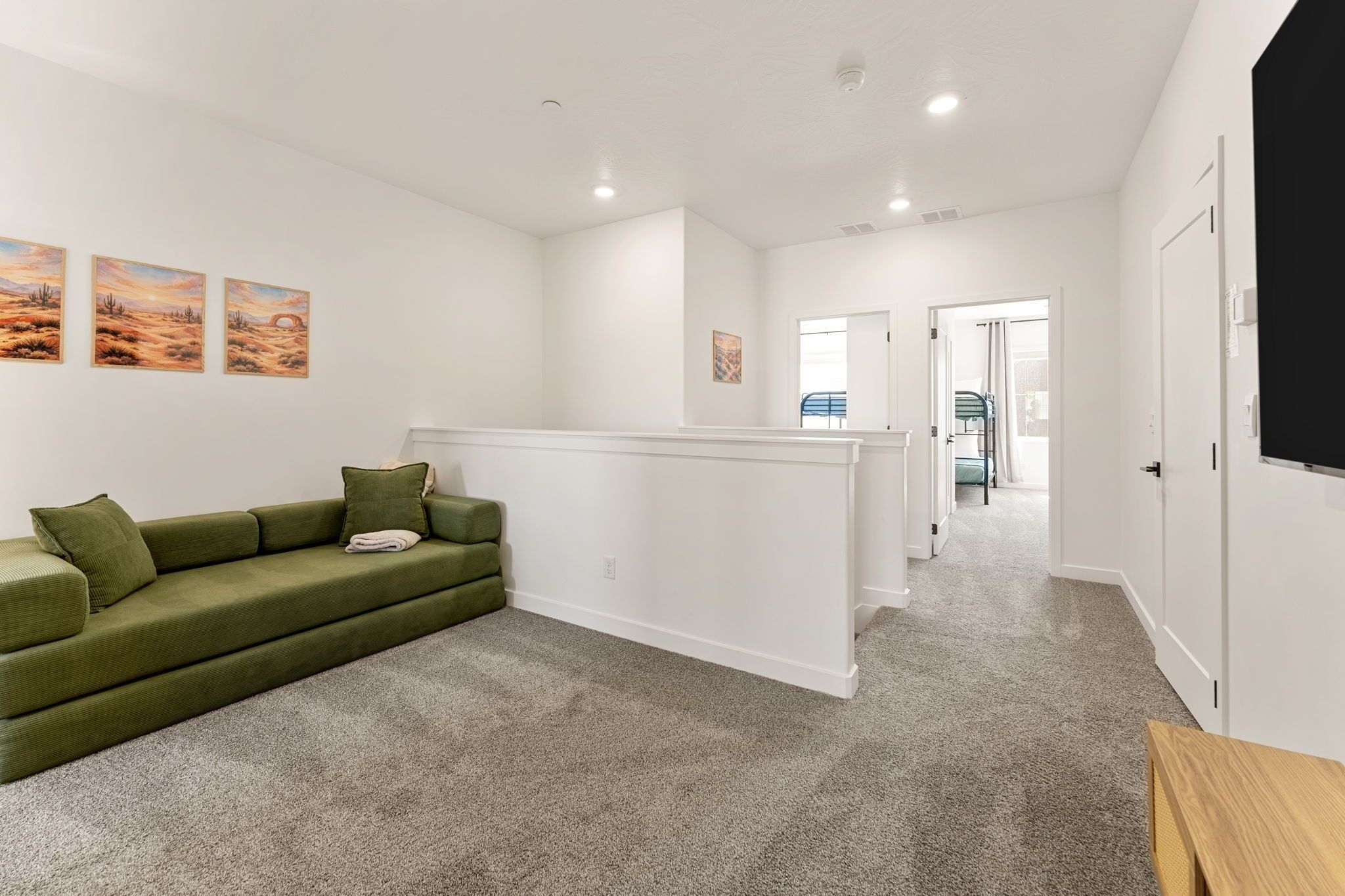 A modern living room with a green sofa, a white partition, and a view into another room.